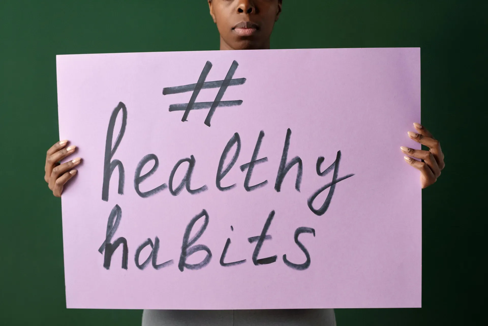 A person holds up a hand-lettered placard reading 'healthy habits' against a dark green wall