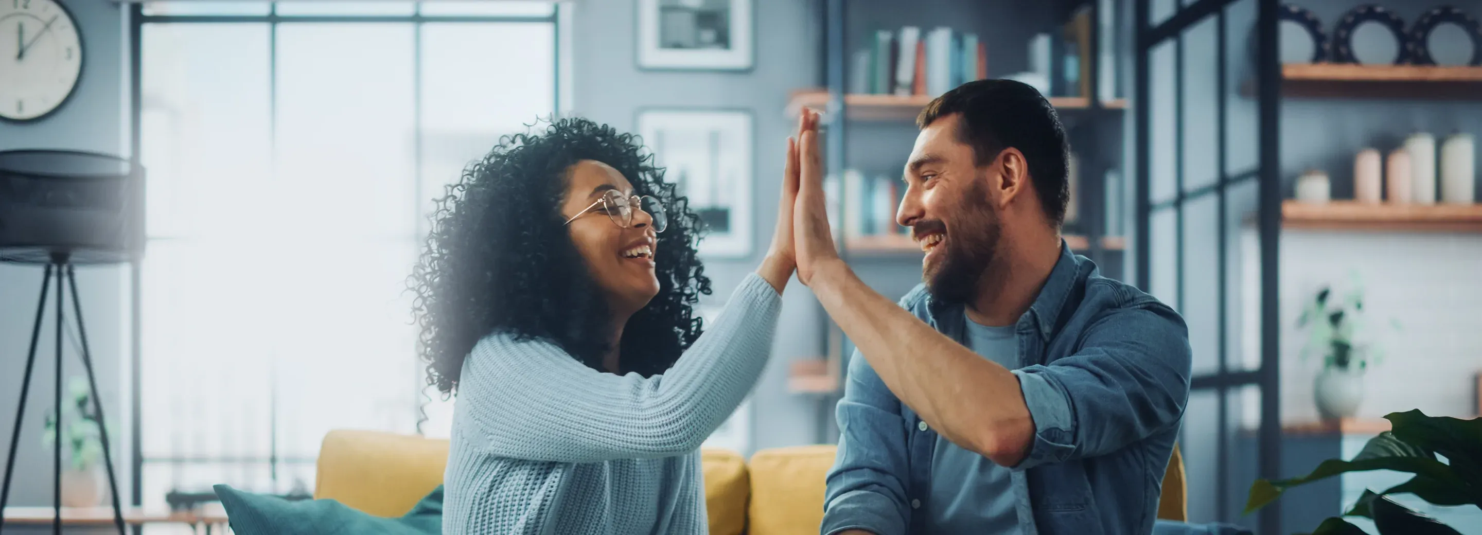 Two people smiling and high-fiving while relaxing at home