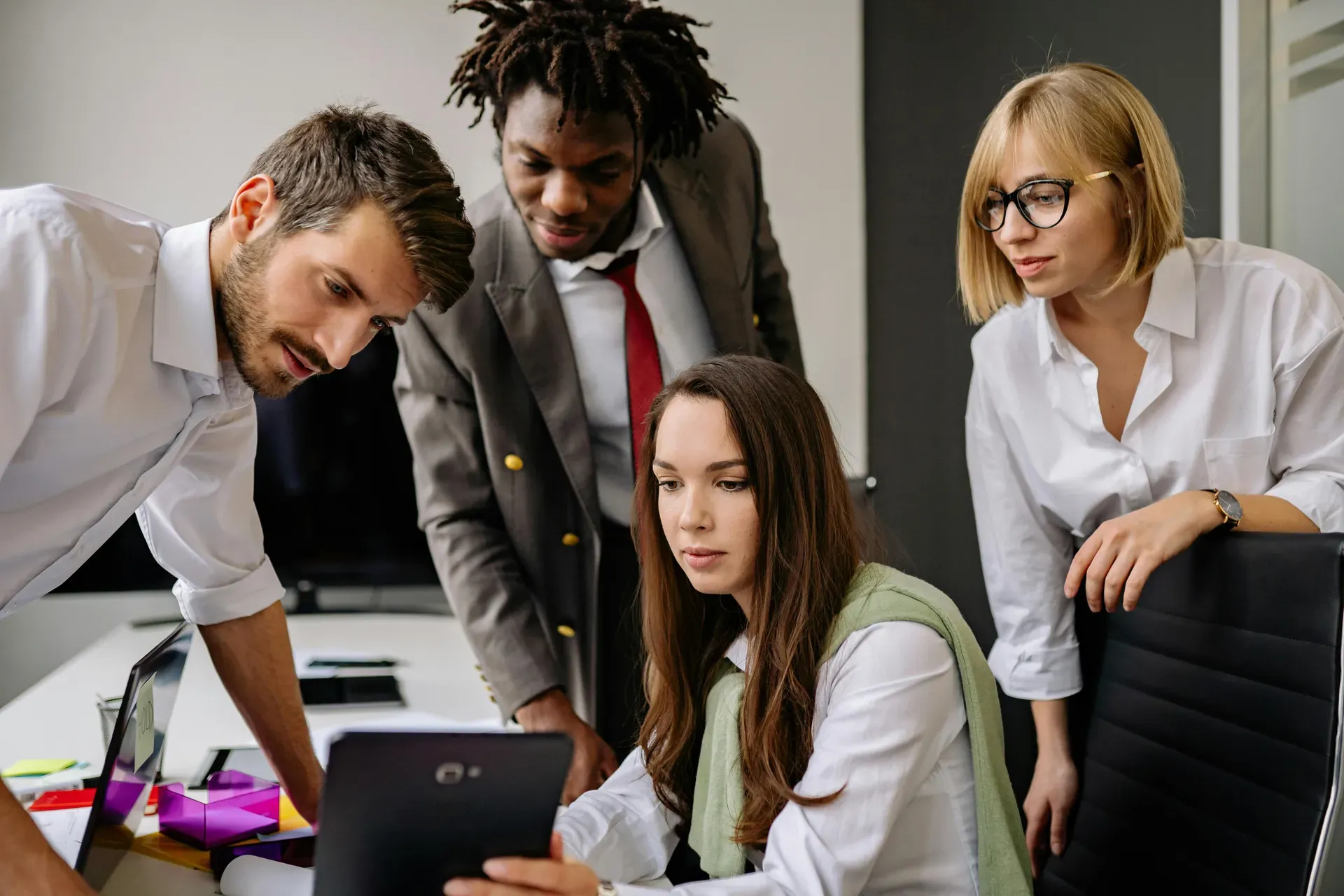 Four colleagues lean in together to look at a tablet held by a woman seated at a desk