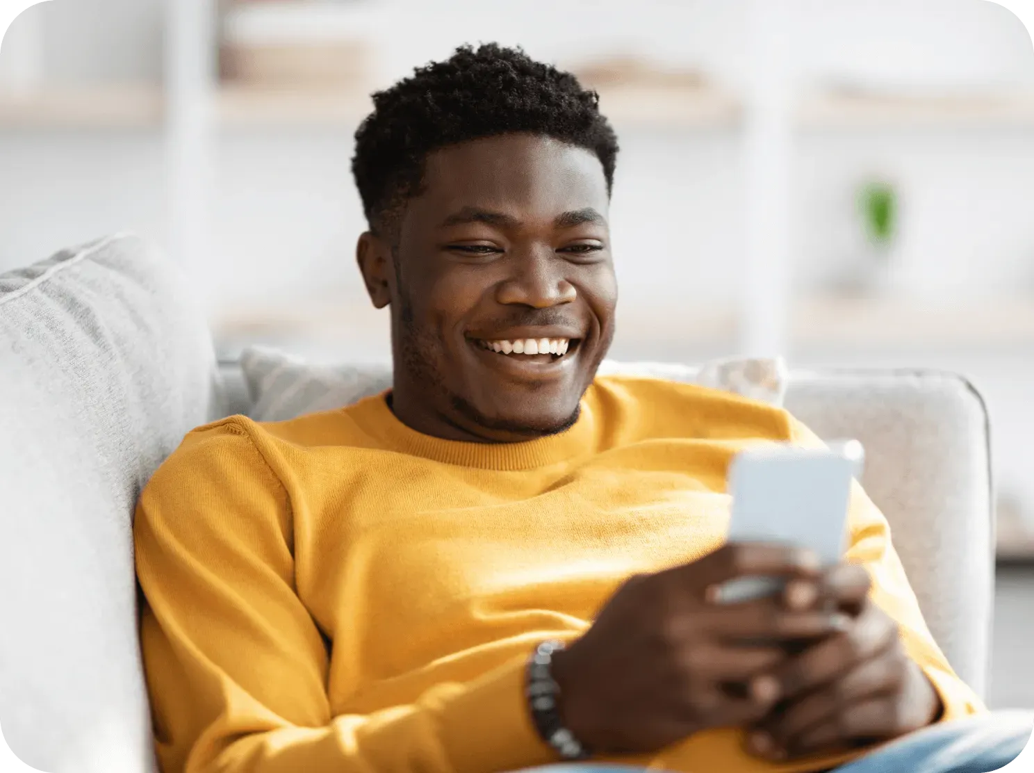 A smiling man relaxing on a couch while using the Yuna app on his phone